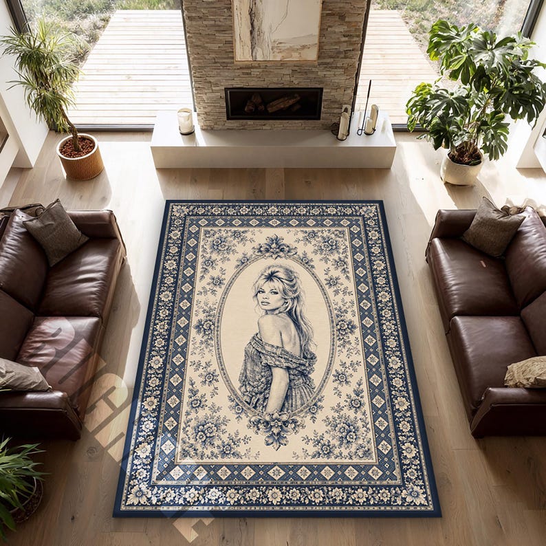 May include: A rectangular area rug with a cream-colored background and a blue floral border. The rug features an oval portrait of a woman in a blue dress. The rug is placed in a living room with leather sofas and a fireplace.