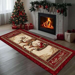 Op de afbeelding: Een rechthoekig kersttapijt met een rode rand en een cr&egrave;mekleurig midden. Het midden toont een feestelijke illustratie van de kerstman in een slee getrokken door rendieren. Het tapijt ligt voor een open haard en een kerstboom.