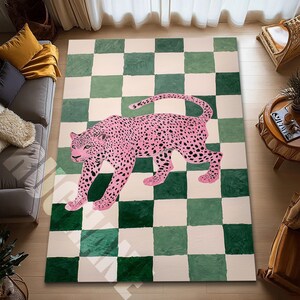 May include: A rectangular area rug with a pink leopard design on a green and white checkered background. The leopard has black spots and is walking across the rug. The rug is placed on a wooden floor.