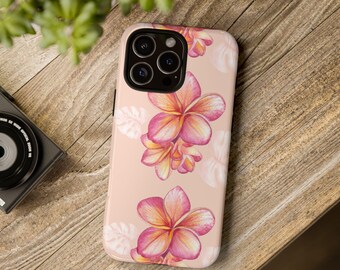 May include: A phone case with a floral design. The case is a light peach color and features a cluster of pink and yellow plumeria flowers. White leaves are scattered around the flowers. The phone case is on a wooden surface.