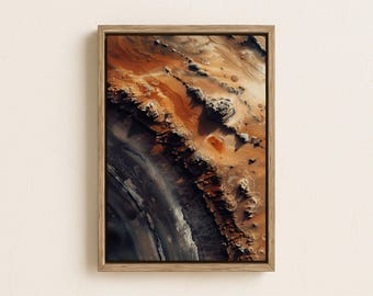 May include: Abstract art print in a wooden frame. The artwork depicts a textured, aerial view of a landscape with shades of brown, orange, and grey. The composition evokes a sense of depth and geological formations.