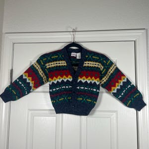 May include: A navy blue cardigan sweater with a colorful geometric pattern. The pattern includes red, yellow, green, and white shapes. The sweater has a V-neck and button closure.