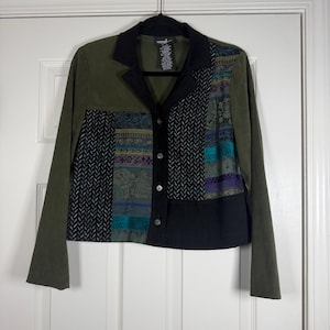 May include: Olive green jacket with a patchwork design. The jacket features a black collar and button closure. The patchwork includes teal, purple, and black patterned fabrics. The sleeves are a solid olive green.