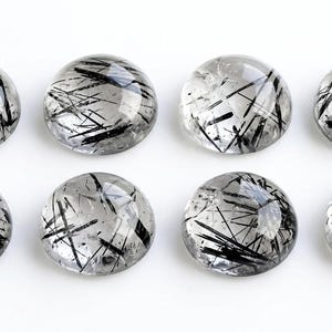 Pode incluir: Oito pedras preciosas de quartzo rutilado com corte cabochão redondo, dispostas em duas filas de quatro. Cada pedra transparente e polida apresenta distintas inclusões pretas em forma de agulha de rutilo no seu interior.