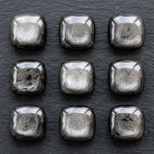 May include: Nine square-shaped, polished metallic hematite stones arranged in a three-by-three grid. Each stone features a smooth, rounded surface with a reflective, gunmetal grey finish and subtle, natural variations in texture and dark inclusions.