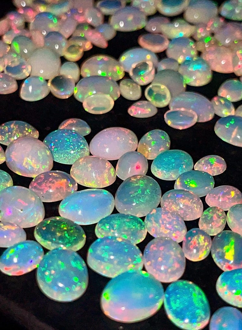 May include: A collection of polished opals in various sizes and shapes. The opals display a range of colors, including iridescent blues, greens, pinks, and yellows, with a luminous, gem-like quality. The opals are set against a dark background.