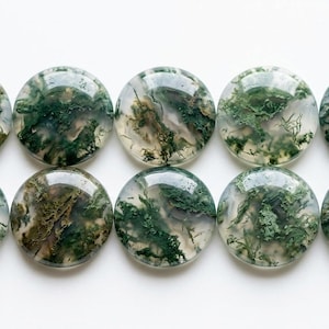 May include: Ten round, polished moss agate cabochons. Each stone has a translucent base with intricate patterns of green, brown, and white, resembling miniature landscapes. The cabochons are approximately 2.5 cm in diameter.