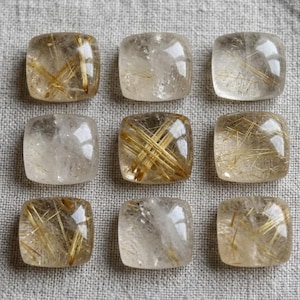 Puede incluir: Nueve piedras preciosas de cuarzo rutilado de forma cuadrada dispuestas en una cuadrícula de tres por tres. Cada piedra translúcida presenta una superficie lisa y pulida con inclusiones doradas en forma de aguja dentro de la estructura.
