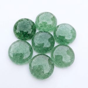 Puede incluir: Un conjunto de siete piedras de aventurina verde, lisas y circulares, dispuestas en racimo. Cada piedra presenta una superficie pulida y brillante con inclusiones internas naturales y tonos variados de verde bosque translúcido.