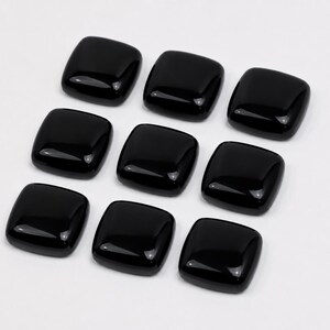 May include: A collection of nine individual black square buttons with rounded corners and a smooth, glossy finish. Each button features a slightly domed surface that reflects light, creating a uniform appearance across the entire set of items.