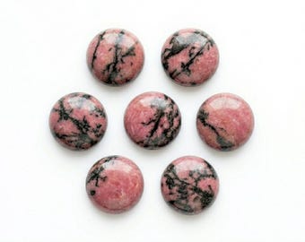 May include: Seven round, polished rhodonite gemstones arranged in a circular pattern on a white background. The stones are a mix of pink and black, with a marbled appearance. These gemstones are ideal for jewelry making or collecting.