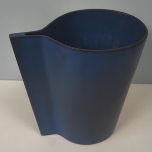 Może przedstawiać: Dzbanek ceramiczny w kolorze głębokiego błękitu z matowym wykończeniem i ciemną krawędzią. Naczynie posiada szeroki, otwarty wierzch z wyraźnym, zintegrowanym dzióbkiem do nalewania z jednej strony oraz gładki, zakrzywiony korpus zwężający się ku podstawie.