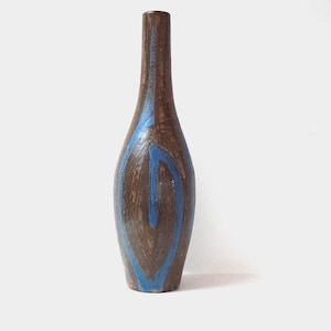 Op de afbeelding: Een bruine keramische vaas met een blauw abstract ontwerp. De vaas heeft een slanke hals en een afgeronde body. Het blauwe ontwerp is een verticale lijn die uitloopt in een druppelvorm. De vaas staat op een wit oppervlak.