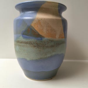 Könnte beinhalten: Eine Keramikvase mit ausgestelltem Rand und abgerundetem Körper, die eine mehrfarbige Glasur in den Tönen Immergrünblau, sanftem Pfirsich und gedämpftem Salbeigrün aufweist. Die Oberfläche hat eine glatte Textur mit sichtbaren Farbübergängen.