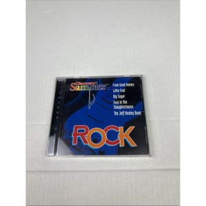 May include: A compact disc titled "Discovery Sampler Rock" featuring a blue guitar graphic. The CD case displays the names of several bands, including "From Good Homes" and "The Jeff Healey Band."