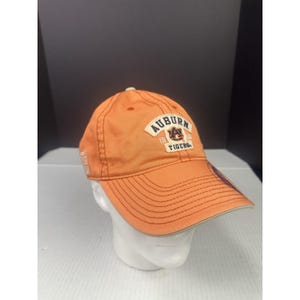 May include: Orange baseball cap with the word "AUBURN" in white lettering. The cap features the Auburn Tigers logo and the years 1856 and 1956. The cap has a curved brim and a stitched design.