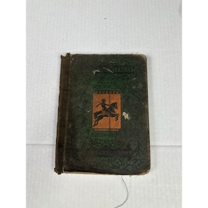 May include: Antique book with a dark green cover featuring the title "Our Readers Primer" and an illustration of a person on a horse. The book has a worn appearance, with visible signs of age and use. The cover has decorative floral patterns.