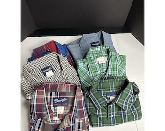Könnte beinhalten: Eine Sammlung gefalteter Wrangler-Hemden in verschiedenen Farben und Mustern. Die Hemden umfassen Karomuster, Vichy-Muster und unifarbene Designs, wobei das Wrangler-Logo auf einigen sichtbar ist. Die Hemden sind ordentlich gestapelt und zeigen eine Vielzahl von Stilen.
