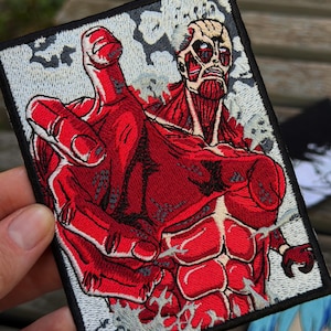 May include: A rectangular embroidered patch featuring a red, muscular humanoid figure with exposed muscle fibres and a skeletal face. The figure is reaching forward with a large hand against a background of grey and white clouds with a black border.