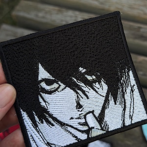 Op de afbeelding: Een vierkante geborduurde patch met een zwart-witte grafische illustratie van een personage met donker haar, intense ogen en een vinger bij de mond. Het ontwerp is uitgevoerd in contrastrijk garen met een dikke zwarte rand.