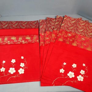 May include: A set of red placemats with a floral design. The placemats have a white flower and stem design on the bottom half. The top half of the placemats have a gold paisley design. The placemats are rectangular.
