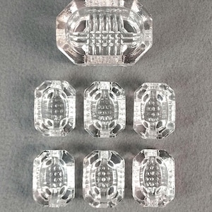 May include: A set of seven clear, faceted glass cabinet knobs. One larger knob is rectangular with an octagonal top, and six smaller knobs are rectangular with rounded ends. The knobs have a detailed, textured design.