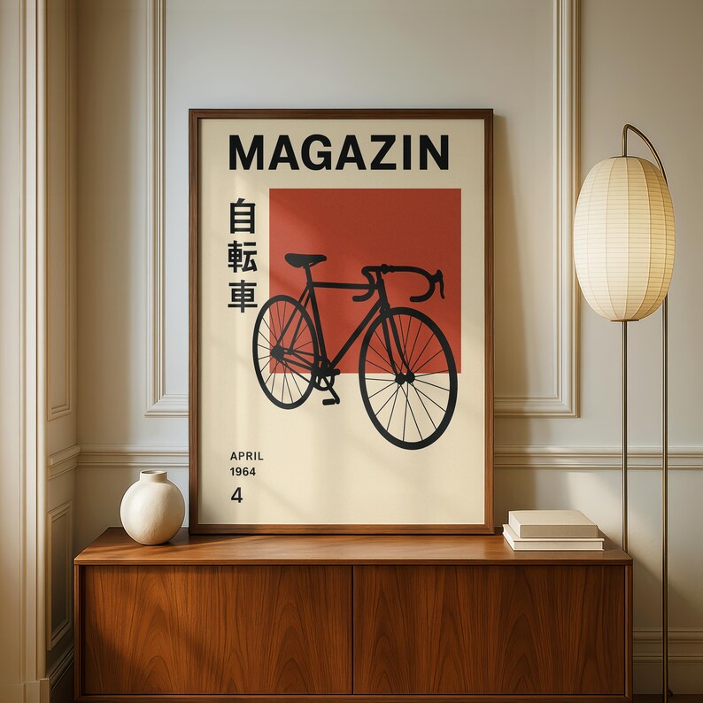 May include: A framed poster with a black bicycle illustration against a red backdrop, with the word "MAGAZIN" above and Japanese characters and the words "APRIL 1964 4" below. The poster is in a wooden frame and sits on a wooden cabinet.