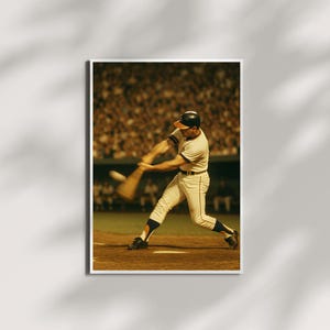 Könnte beinhalten: Vintage Baseball-Actionaufnahme. Ein Schlagmann in cremefarbener Uniform mit schwarzen Akzenten schwingt einen Holzschläger. Der Hintergrund zeigt ein volles Stadion mit verschwommener Menge, beleuchtet von Stadionlichtern. Das Bild ist in einem weißen Rahmen gerahmt.