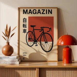 May include: A framed poster with the word "MAGAZIN" at the top, featuring a black bicycle illustration on a red background. The poster also includes Japanese characters and the date "APRIL 1964". A red lamp and a brown vase are on a wooden cabinet.
