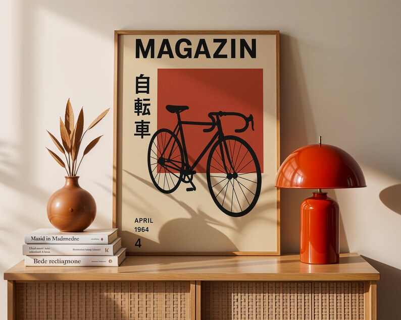 May include: A framed poster with the word "MAGAZIN" at the top, featuring a black bicycle illustration on a red background. The poster also includes Japanese characters and the date "APRIL 1964". A red lamp and a brown vase are on a wooden cabinet.