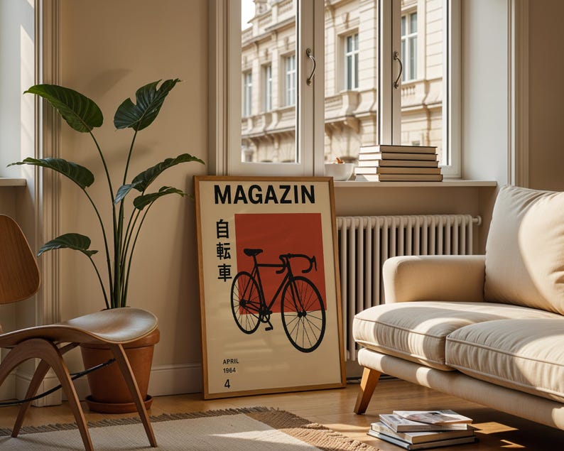 May include: A framed poster with the word "MAGAZIN" and Japanese characters, featuring a black bicycle illustration on a red and beige background. The poster is displayed in a living room with a beige sofa, wooden chair, and a large potted plant.