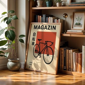 May include: A framed poster with the word "MAGAZIN" in black, featuring a black bicycle illustration on a cream background with a red rectangle. Japanese text and the date "APRIL 1964" are also visible. The poster is displayed on a wooden bookshelf.
