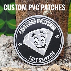 Puede incluir: Un parche redondo de PVC en blanco y negro con el texto "CUSTOM PATCHES" y "FREE SHIPPING". El parche presenta un gráfico de diamante sonriente. Las letras "CA" y "SD" también son visibles en el parche.