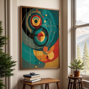 May include: Abstract art print in a wooden frame. The artwork features concentric circles and geometric shapes in teal, red, yellow, and black. The print hangs above a wooden table with books and a camera.