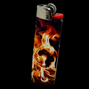 Puede incluir: Un encendedor negro y plateado con un vibrante dise&ntilde;o de llamas en tonos naranja y amarillo. El encendedor tiene un bot&oacute;n de encendido rojo y una parte superior plateada met&aacute;lica. El gr&aacute;fico de la llama cubre el cuerpo del encendedor.