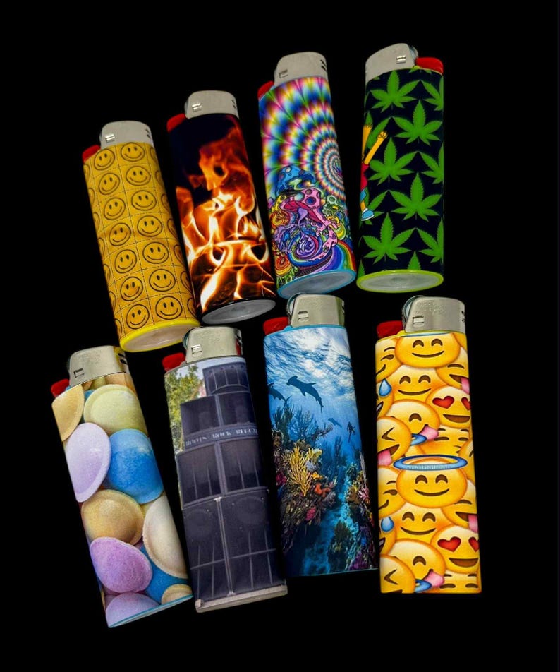 May include: A collection of eight lighters with various designs. The lighters feature images such as smiley faces, flames, a psychedelic swirl, cannabis leaves, colorful candies, a stack of speakers, an underwater scene with dolphins, and emoji faces.