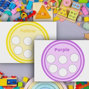 May include: Two educational cards with a circle design and six white circles. One card is yellow with the word "Yellow", and the other is purple with the word "Purple". The cards are surrounded by colorful wooden toys.