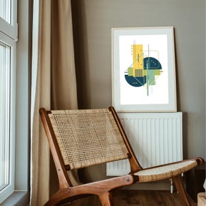 May include: A framed abstract art print featuring geometric shapes in yellow, teal, and navy blue against a white background. The artwork is displayed on a white radiator, next to a wooden chair with a woven seat and back.