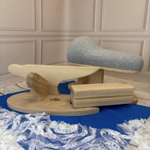 May include: A set of light-colored wooden sewing tools including a tailor's clapper, a sleeve board, and a curved pressing ham covered in heather gray fabric. The wooden pieces feature a natural grain finish and the text Needle Craft is visible.