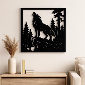 Può includere: Arte da parete in metallo nero raffigurante la silhouette di un lupo che ulula su uno sfondo di foresta. L'opera è incorniciata e montata su una parete bianca, creando un contrasto sorprendente. Il lupo è su un affioramento roccioso, circondato da pini stilizzati.