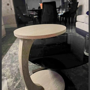 May include: A beige stone side table with a circular top and base, connected by a curved support. The table is approximately 24 inches in height and 18 inches in diameter.