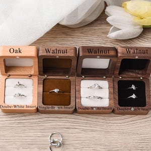 May include: Wooden ring boxes in oak and walnut, each with a hinged lid. The boxes contain rings with clear stones, displayed on white, brown, and black inserts. Text on the boxes reads "Oak" and "Walnut".