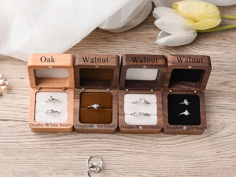 May include: Wooden ring boxes in oak and walnut, each with a hinged lid. The boxes contain rings with clear stones, displayed on white, brown, and black inserts. Text on the boxes reads "Oak" and "Walnut".