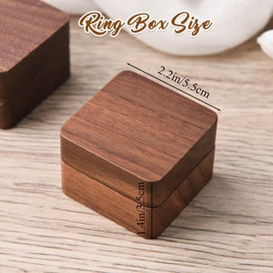 May include: A square wooden ring box with a rich brown finish. The box measures 2.2 inches (5.5 cm) wide and 1.4 inches (3.5 cm) high. The text "Ring Box Size" is displayed above the box.