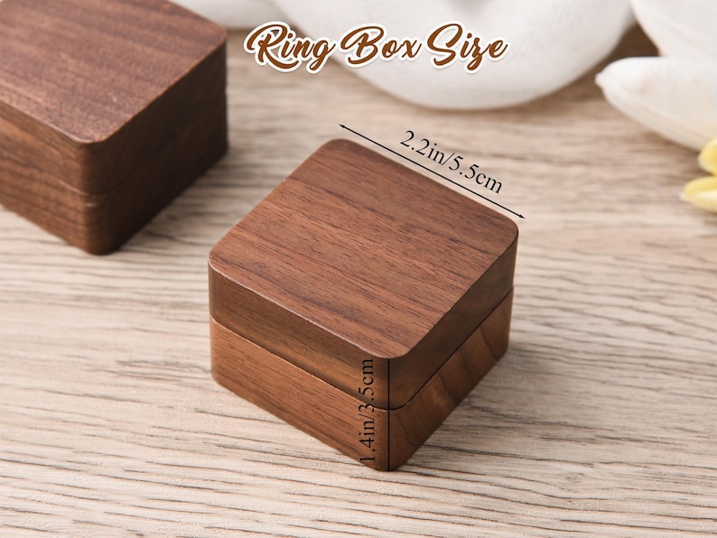 May include: A square wooden ring box with a rich brown finish. The box measures 2.2 inches (5.5 cm) wide and 1.4 inches (3.5 cm) high. The text "Ring Box Size" is displayed above the box.