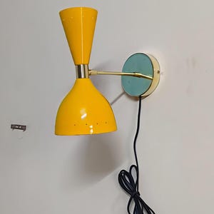 Può includere: Applique da parete giallo in stile moderno della metà del secolo, con paralume conico e piastra di montaggio turchese. La lampada ha un braccio in ottone e un cavo di alimentazione nero. L'applique è montata su una parete bianca.