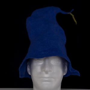 May include: A vibrant blue felt hat with a tall, slightly curved, and pointed crown that tapers toward the top. The hat features a wide, flexible brim that flares outward at the base, creating a distinct silhouette against the dark background.