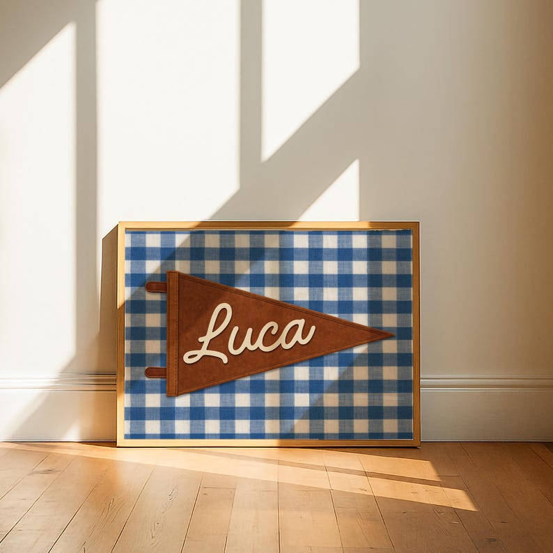 May include: A framed wall art piece featuring a brown pennant with the name "Luca" in white script. The pennant is set against a blue and white gingham pattern background. The frame is a light wood color.