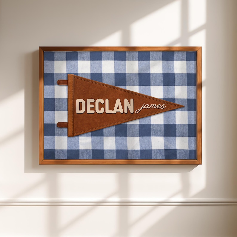 May include: A framed wall art piece featuring a blue and white gingham pattern. A brown pennant with the name "DECLAN james" is centered on the artwork. The frame is made of wood.