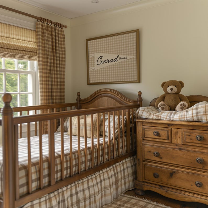 May include: A wooden crib with a brown and white checkered sheet and skirt, positioned next to a wooden dresser with a brown teddy bear. A framed wall print features a pennant design with the text Conrad Hayes in a brown checkered background.
